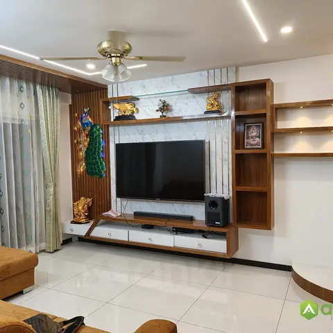 Marble-effect TV feature wall with vertical brass inlay strips flanked by wood display cubbies, styled with gold Indian statuettes and a peacock wall ornament