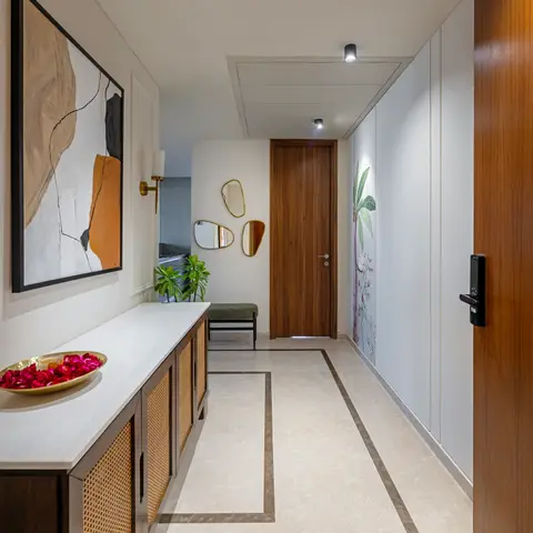 Marble-floored entrance foyer with a walnut main door, digital smart lock, a rattan-front console beneath abstract art, and a trio of asymmetric brass mirrors.