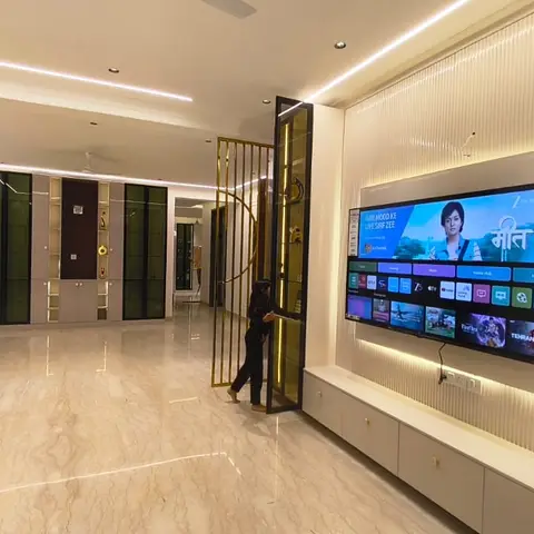 Marble-floored living area with a backlit fluted TV feature wall and a brass jaali screen dividing it from the entrance foyer.