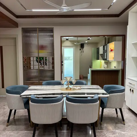 Marble-top dining table for eight with blue and cream ribbed-velvet chairs under a cove-lit false ceiling