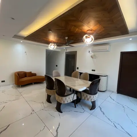 Marble-top dining table with dark wood tufted chairs beneath a chevron-pattern wood-clad false ceiling and twin globe pendant lights