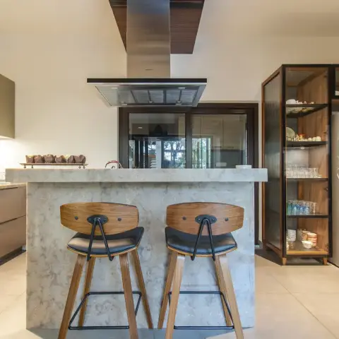 Marble waterfall breakfast island with two walnut-and-black-leather stools, a stainless island chimney dropping out of a walnut ceiling raft