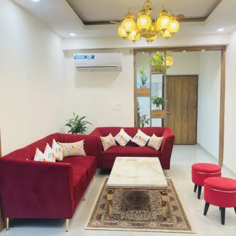 Maroon velvet L-shaped sofa with a marble-top gold-leg coffee table under a lantern-style jharokha chandelier.