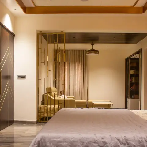 Master bedroom shot from the foot of the bed through a floor-to-ceiling brass fin screen into an attached sitting alcove with two tub chairs
