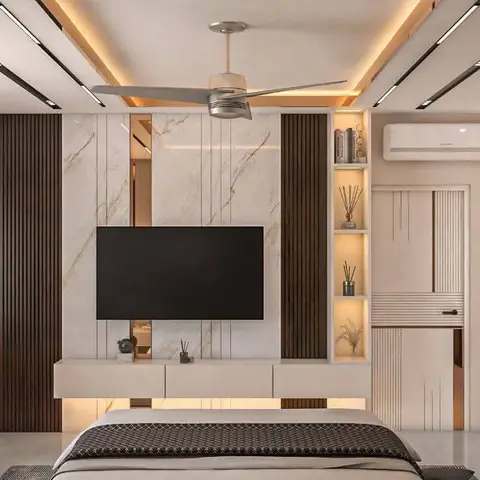 Master bedroom TV wall combining book-matched marble with fluted wood panelling, a backlit display niche, and a cove-lit ceiling with a fan.