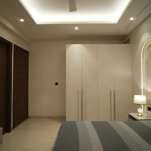 Master bedroom with a backlit LED headboard trim, cream cove-lit ceiling, full-height wardrobes and twin dark-wood doors leading off the room.