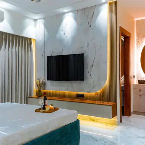 Master bedroom with a book-matched marble TV wall framed by a curved brass-fluted border, a floating walnut console with cove lighting