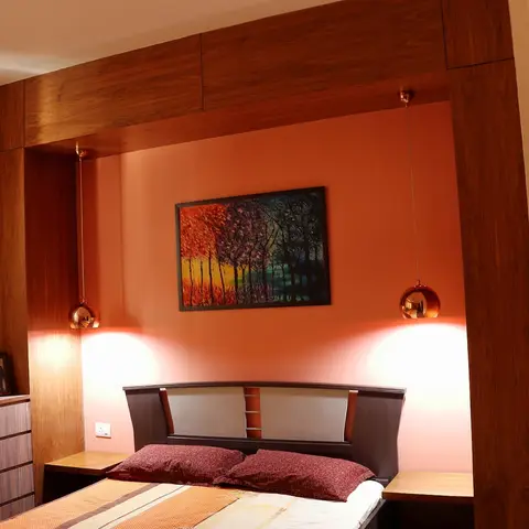 Master bedroom with a burnt-orange accent wall framed by a wood archway, twin globe pendant lights flanking the bed