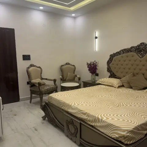 Master bedroom with a carved wood tufted-headboard bed, matching carved armchairs, and a cove-lit box ceiling with a wall-mounted linear light.
