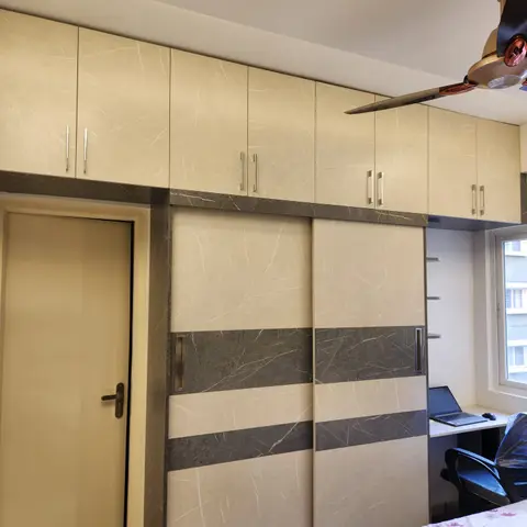 Master bedroom with a cream-and-grey marble-pattern sliding wardrobe, overhead loft cabinets, and a built-in study desk by the window.