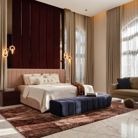 Master bedroom with a deep maroon channel-panelled wall behind a blush upholstered headboard, a navy channel-tufted bench at the foot of the bed