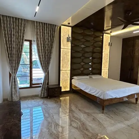 Master bedroom with a diamond-quilted upholstered headboard wall flanked by backlit onyx-look stone pillars under an extended dark wood ceiling soffit