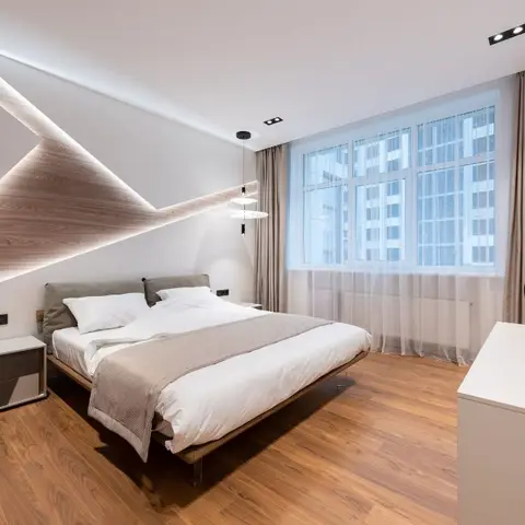 Master bedroom with a dramatic angular wood accent wall traced in backlit LED strips above a floating platform bed, wood flooring