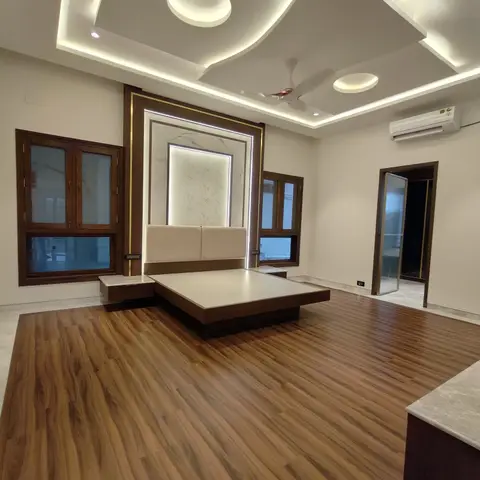 Master bedroom with a floating wood platform bed against a backlit marble headboard wall under a multi-level cove-lit ceiling
