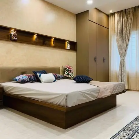 Master bedroom with a floating wood-platform bed and upholstered headboard, a textured wall with a lit display niche for idol figurines, a wardrobe