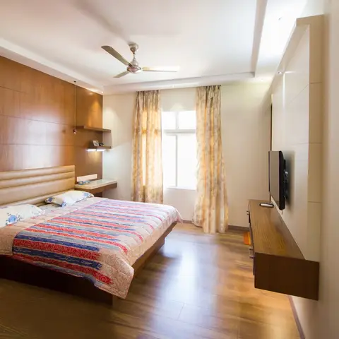 Master bedroom with a full-height teak veneer headboard wall and a channel-tufted beige headboard, twin copper pendant drops serving as bedside lights