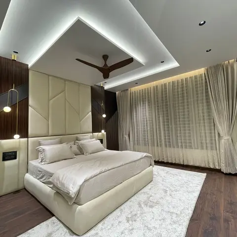 Master bedroom with a geometric channel-tufted cream headboard wall that extends up into an angular cove-lit false ceiling