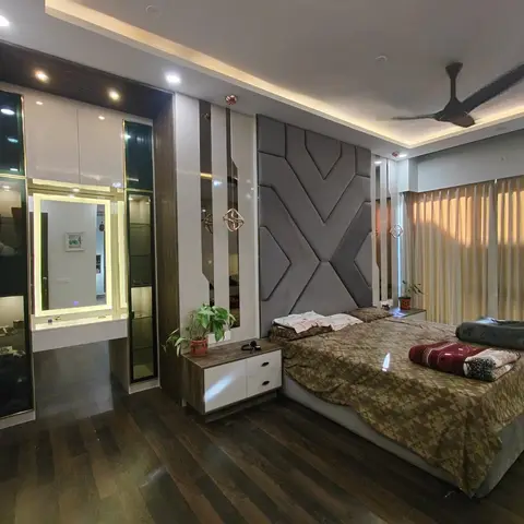 Master bedroom with a grey geometric upholstered headboard wall, rose-gold pendant lights and a mirrored dressing nook in dark wood flooring.