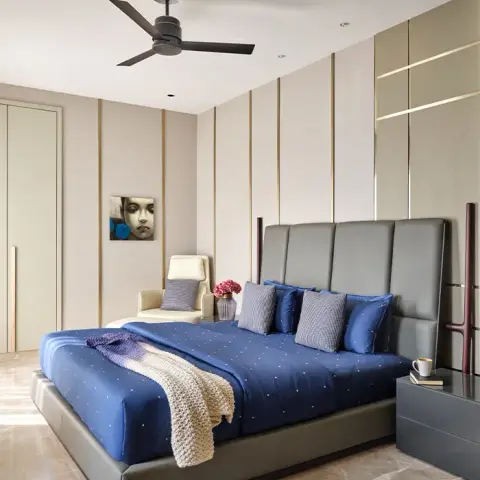 Master bedroom with a grey leather upholstered bed, navy dotted bedding, and a fluted wall panel with brass inlay strips behind a cream accent chair.