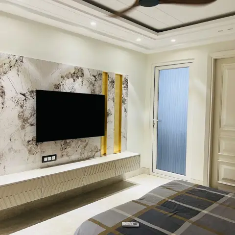 Master bedroom with a marble-panelled TV feature wall framed by gold accent strips, a floating fluted-front console