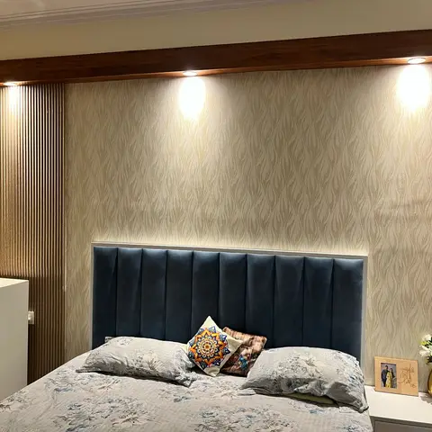 Master bedroom with a navy channel-tufted upholstered headboard against gold shimmer-pattern wallpaper