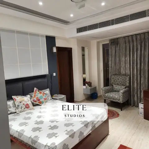 Master bedroom with a padded grid-panel headboard wall, navy velvet bed, floor-length patterned curtains and a diamond-print accent armchair by the window.