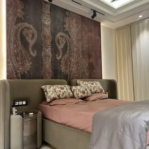 Master bedroom with a paisley wallpaper mural behind an upholstered wingback bed, dusty pink bedding and a matching round nightstand.