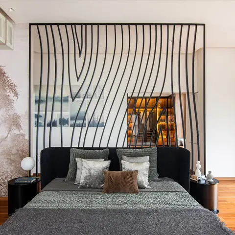 Master bedroom with a sculptural wave-patterned black metal headboard screen framing a glimpse of the attached walk-in wardrobe