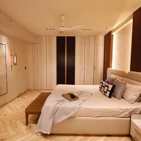 Master bedroom with a striped fluted wardrobe, herringbone wood flooring and an upholstered bed against a backlit textured accent wall.