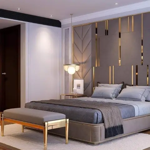 Master bedroom with a taupe upholstered panel wall accented by vertical brass inlay strips and a mirrored gold-trimmed bench at the foot of the bed