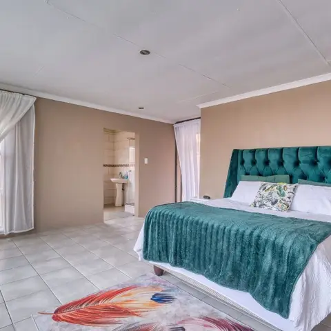 Master bedroom with a teal channel-tufted headboard and matching throw on a white bed, sheer curtains