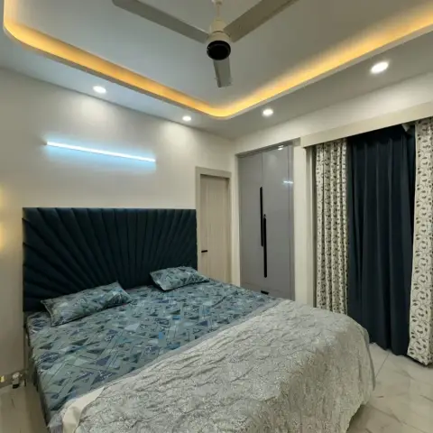 Master bedroom with a teal sunburst-pleated upholstered headboard, warm cove ceiling lighting with a ceiling fan, a glossy grey wardrobe