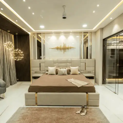 Master bedroom with a tufted gold-trimmed upholstered bed facing a glass-walled dressing room, lit by two spherical string-light pendants.