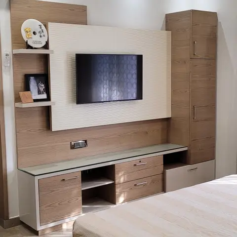 Master bedroom with a wood-veneer TV panel flanked by floating display shelves and a tall wardrobe