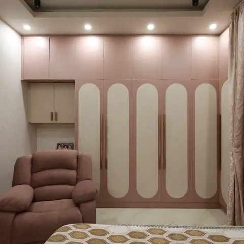 Master bedroom with an arch-pattern blush-pink wardrobe wall, a stepped cove-lit ceiling, and a brown recliner armchair beside the bed.