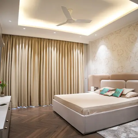 Master bedroom with an upholstered beige wing-headboard bed, a rose-print wallpaper accent wall, herringbone wood flooring, and a cove-lit false ceiling.