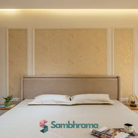 Master bedroom with beige floral wallpaper panels framed in white moulding above an upholstered taupe headboard, matching wood-trimmed wardrobe on the left.