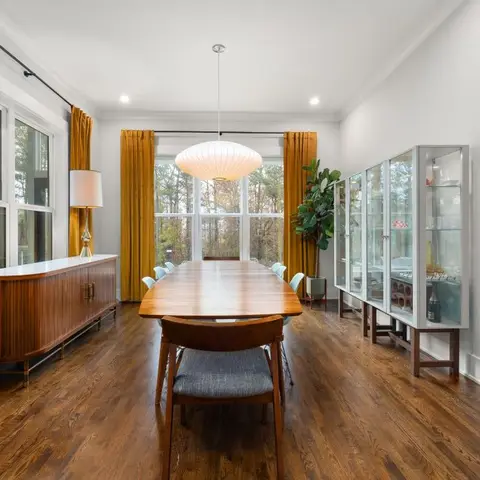 Mid-century dining room with a walnut table and teal chairs beneath a cocoon pendant lamp, framed by floor-length mustard velvet curtains