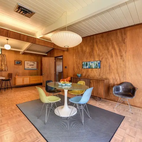 Mid-century dining room with wood-panelled walls, a Nelson-style bubble pendant and multicolor molded shell chairs around a round tulip table