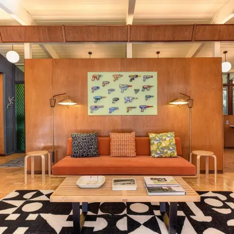 Mid-century living room with a burnt-orange sofa against a wood-panelled divider wall, exposed beam ceiling and a graphic black-and-white rug