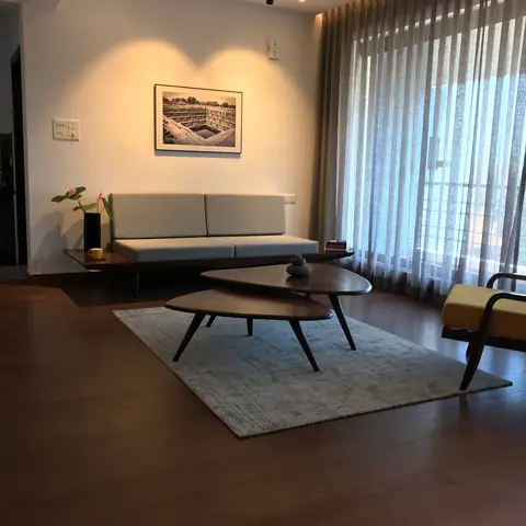 Mid-century living room with a low wood-framed sofa, a mustard-yellow accent armchair, organic-shaped nesting coffee tables on a grey rug