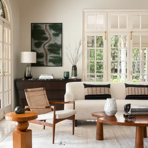 Mid-century living room with a cream boucle sofa, cane-backed wood armchair, dark wood console with framed art