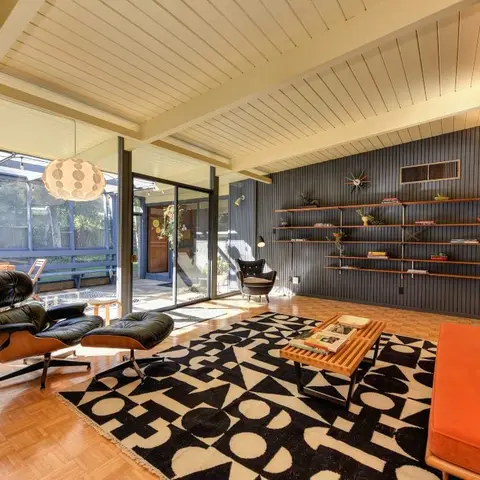 Mid-century living room with an Eames lounge chair and ottoman, exposed wood beam ceiling, navy shiplap wall with floating shelving