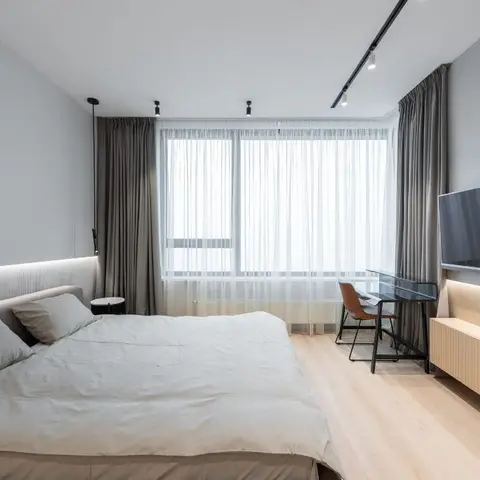 Minimal bedroom with a fluted upholstered headboard wall lit by a cove strip along its base, a floating light-wood TV console