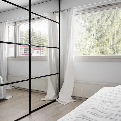 Minimalist bedroom with a black-grid mirrored sliding wardrobe wall reflecting a second bed, white quilted bedding