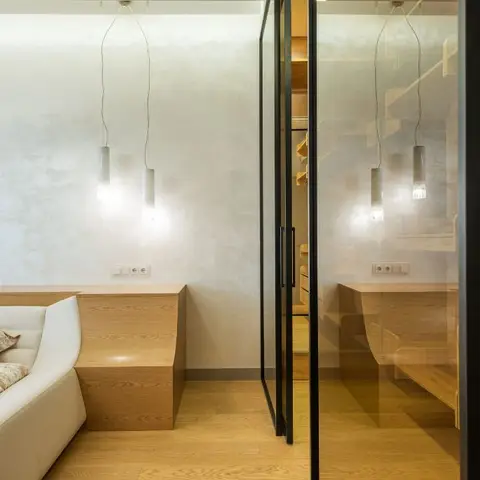 Minimalist bedroom with a curved white leather bed, built-in wood nightstand ledge, twin cylindrical pendant lights, textured plaster wall