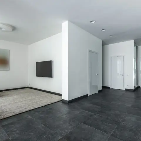 Minimalist living corner with a wall-mounted TV, grey sectional and rug on large-format dark polished tile flooring