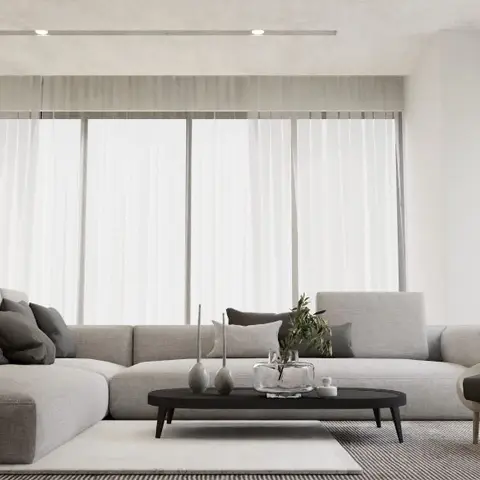 Minimalist living room with a grey L-shaped sectional, a dark oval coffee table, and floor-to-ceiling sheer curtains along the window wall.