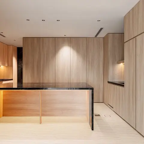 Minimalist wood-veneer kitchen with a black stone waterfall-edge island and full-height handleless cabinetry