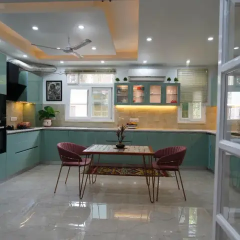 Mint-green U-shaped kitchen seen through open white glazed French doors, with a two-seater breakfast table on a printed kilim runner in the middle of the floor
